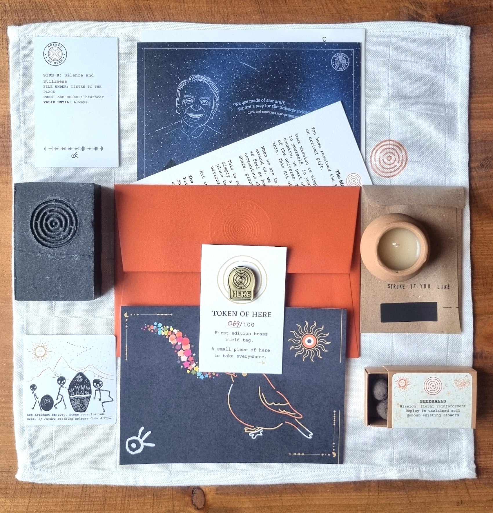 Flatlay showing all objects included in the Kit of Here first edition, including muslin cloth, postcards, candle, soap, seedballs, sticker, matches, QR code, and brass token.