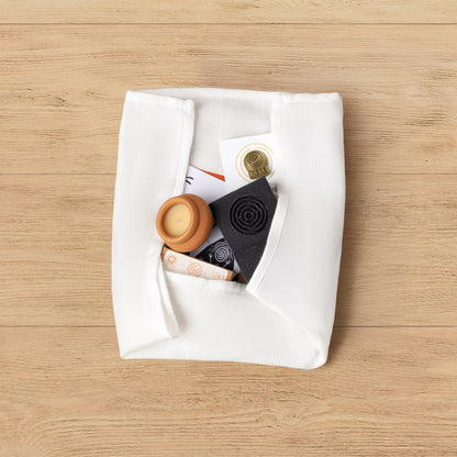 The Kit of Here contents emerging from the muslin cloth wrap, showing the candle, soap, postcards, seedballs, and brass token.