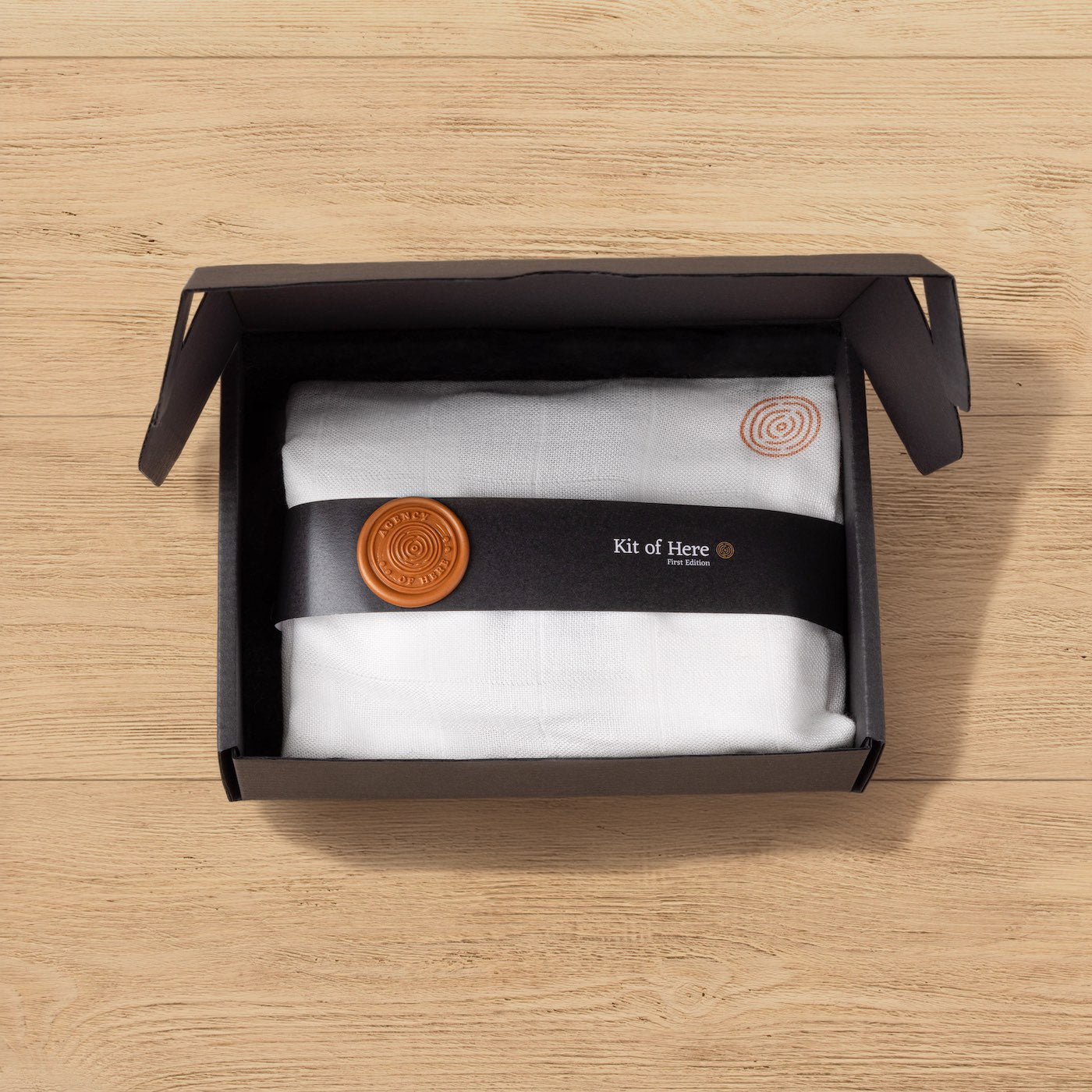 The Kit of Here wrapped in muslin cloth with bellyband and wax seal, presented inside the open box during unboxing.